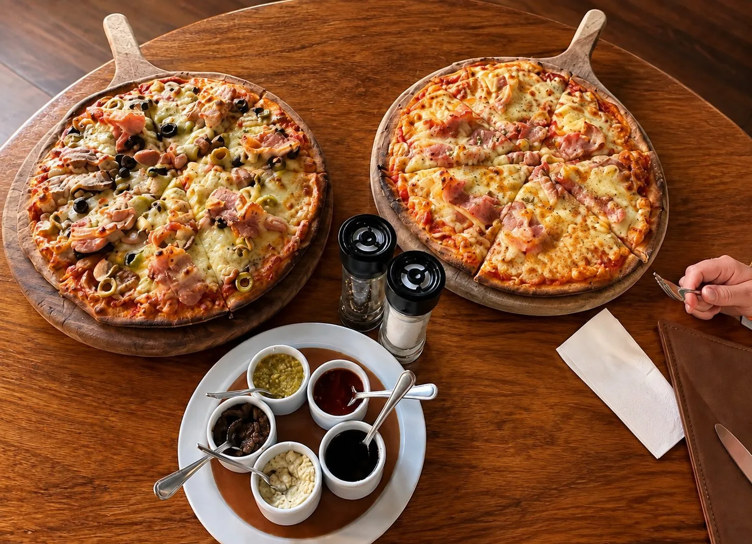Two freshly baked pizzas on wooden boards, with the house sauce board